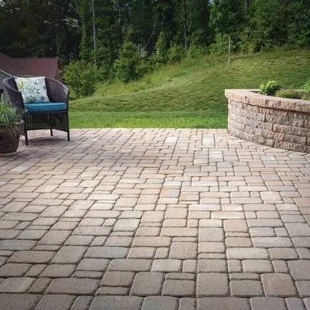 Interlocking multi-tone concrete paver patio with curved stacked-stone retaining wall seating and grassy slope