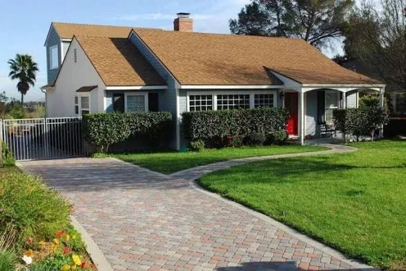 Curved brick-style paver driveway and walkway with wrought-iron gate, green lawn, and clipped hedges