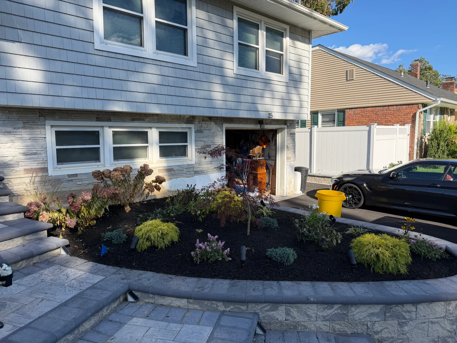 Front yard bed with dark mulch, Japanese maple, gold grasses, and gray paver and stone retaining wall edging