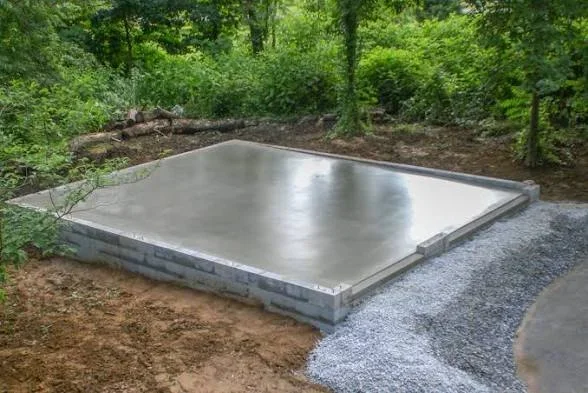 Smooth finished concrete slab on stacked concrete block foundation with gravel edging in a wooded yard