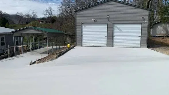 Smooth poured concrete driveway leading to a gray metal garage with two white roll-up doors