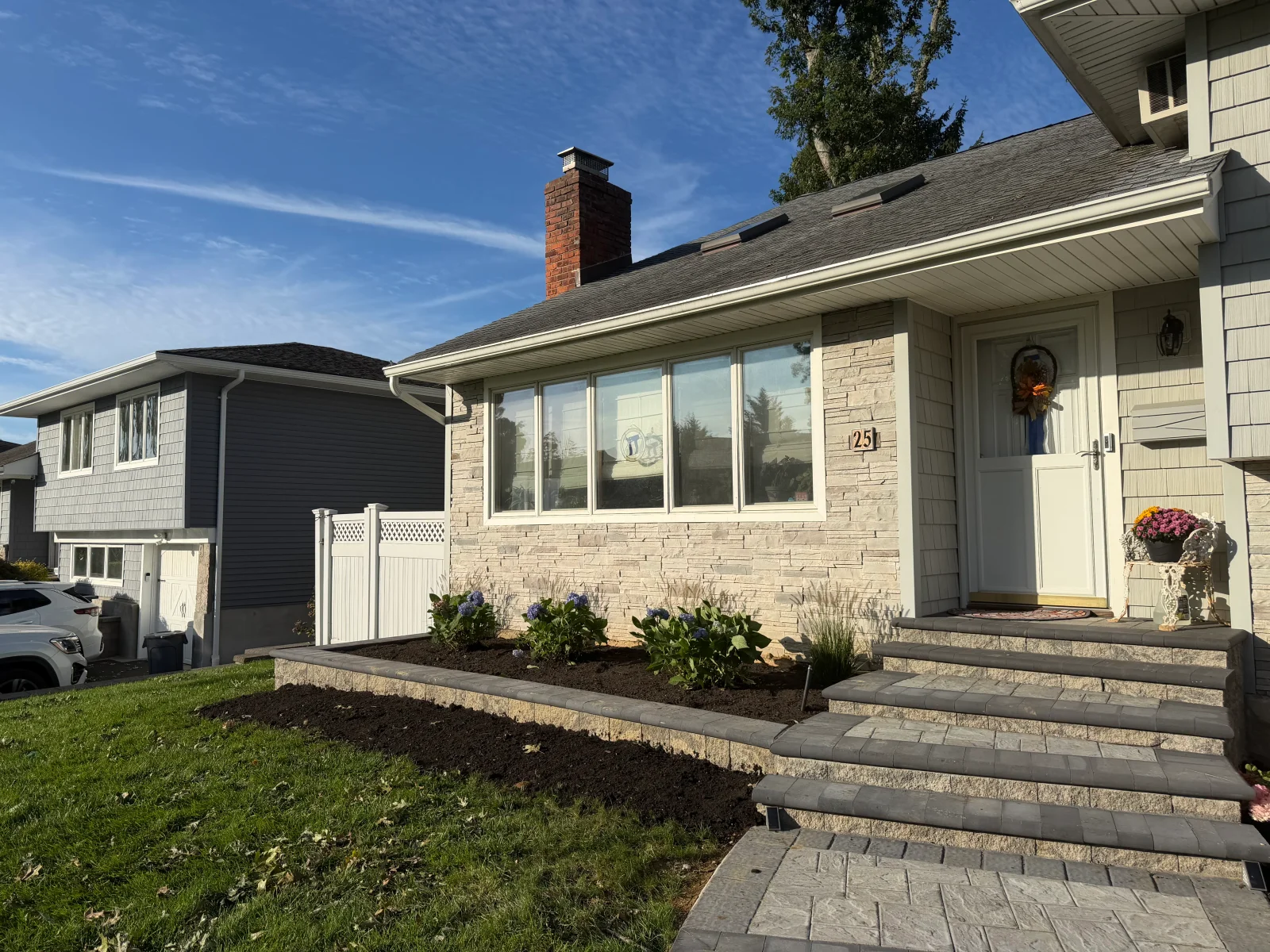 Front entry with paver steps, dark gray interlocking pavers, retaining wall, mulched bed, hydrangeas, and new sod