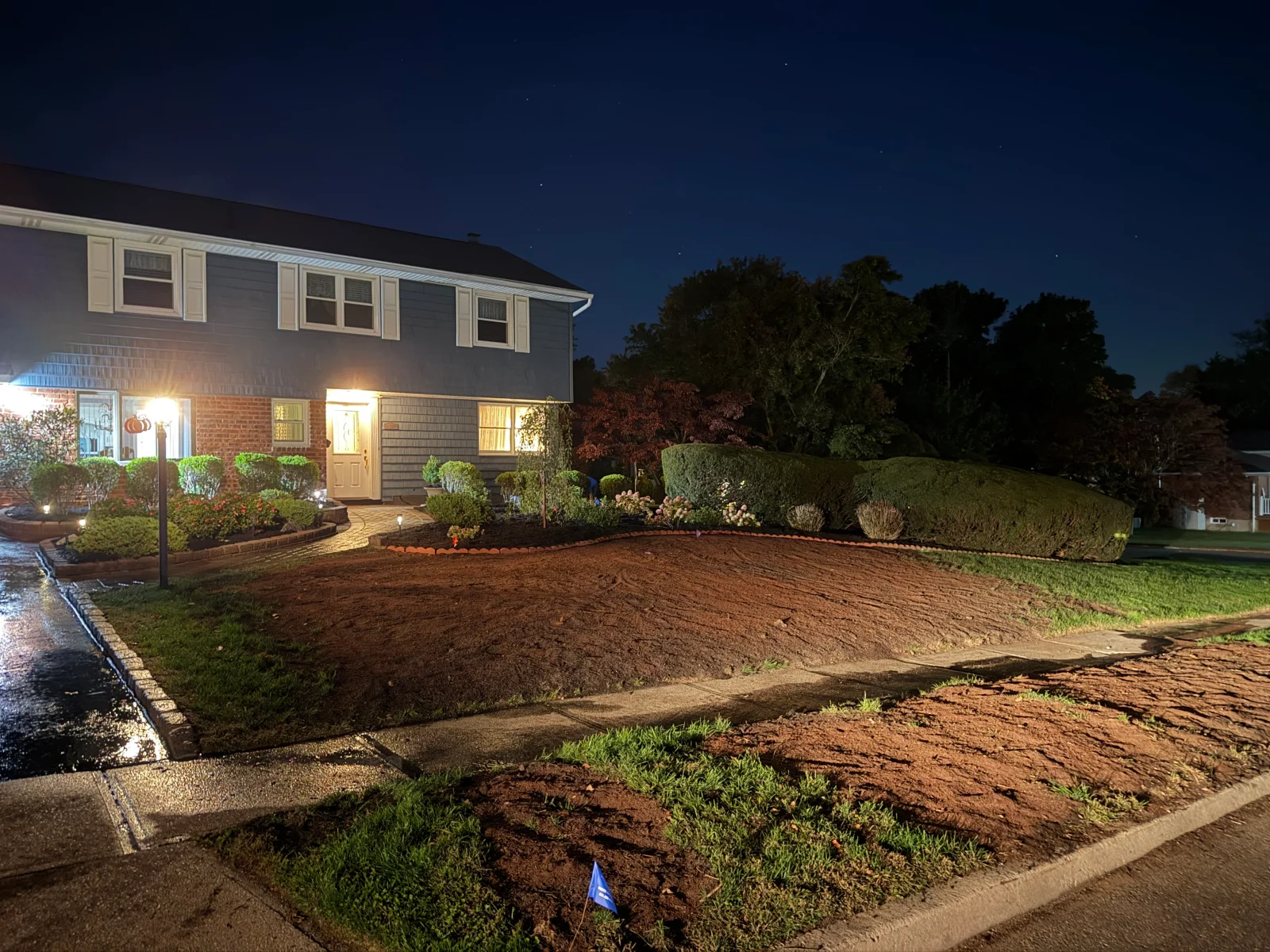 Front yard with freshly graded brown soil, raked surface, existing shrub beds with mulch and brick edging, and sidewalk along the lawn