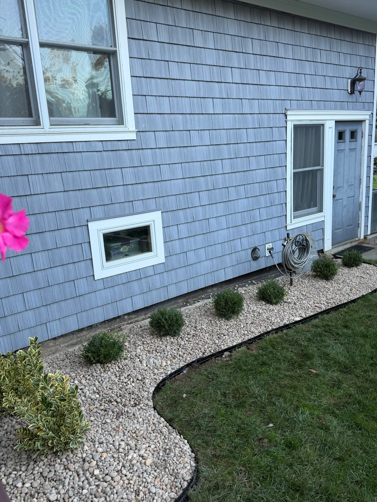 Curved river rock bed with rounded boxwood shrubs and variegated shrub along blue shingle siding foundation