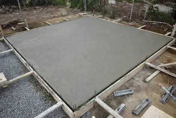 Freshly poured concrete slab inside wood forms with gravel base and rebar edging