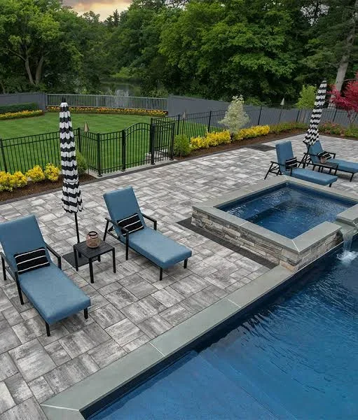 Gray paver patio with in-ground pool, stone-clad spa, blue chaise lounges, and black iron fencing