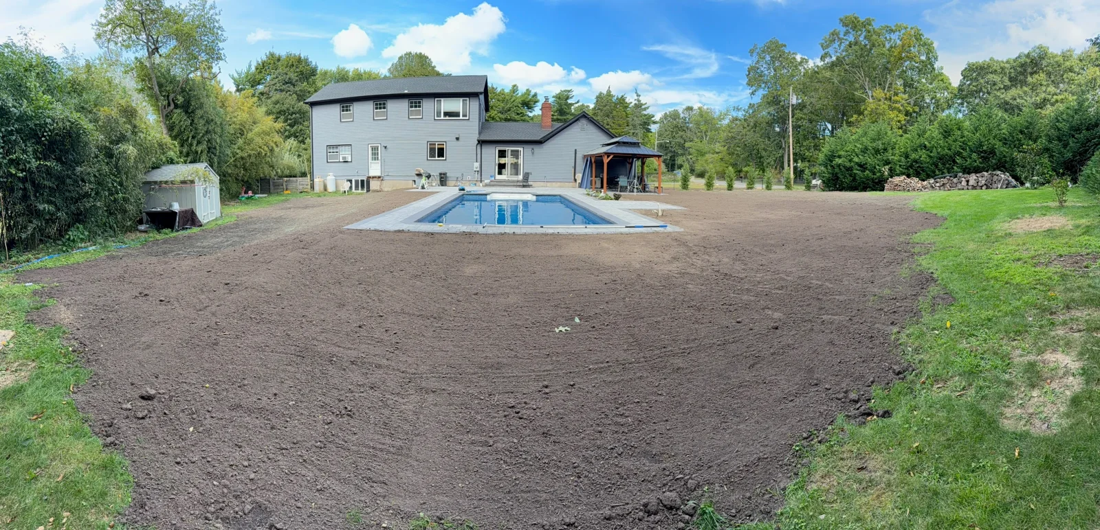 Graded bare topsoil yard beside an in-ground pool with gray coping and a wooden gazebo